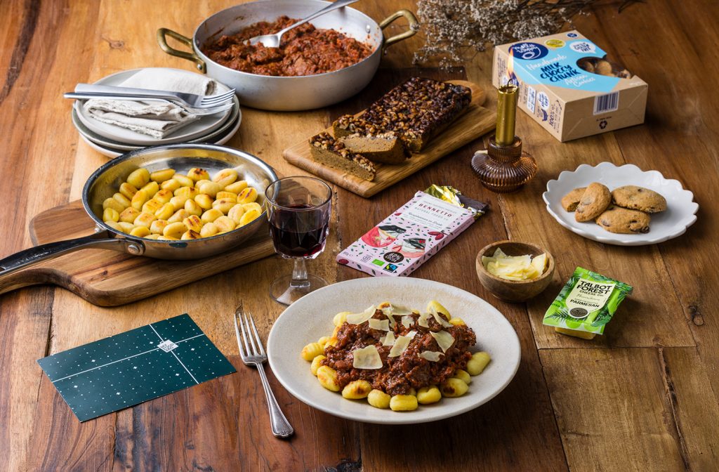 **Gluten free care package with gnocchi, rich tomato ragu, parmesan, cookies, chocolate and treats served on a wooden table.**

A slightly more SEO-focused option:

Gluten free care package featuring gnocchi with ragu, parmesan, cookies, chocolate and gourmet treats for an easy meal at home.
